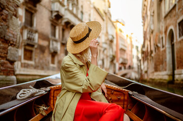 Fototapeta na wymiar Rear, back view of elegant woman wearing straw hat on Gondola ride along beautiful street in Venice, Italy. Travel, vacation, lifestyle conception. Copy, empty space for text