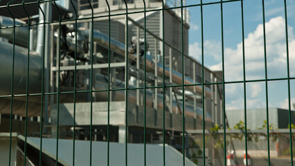 Plakat metal 3D mesh, in the photo a mesh fence in the background is a power plant building and a blue sky