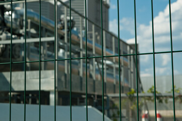 Obraz premium metal 3D mesh, in the photo a mesh fence in the background is a power plant building and a blue sky