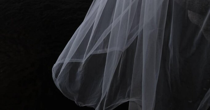 A white translucent veil blowing in the wind. Wedding veil on a dark background. 