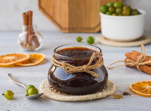 Gooseberry jam in a glass jar on a light wooden background. Preservation, harvest.
