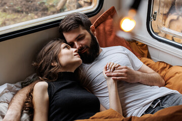 Young beautiful loving couple travelling across country in the van. Millennial man and woman in a travel camper. Cozy atmosphere, vacations vibe