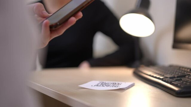 Unrecognizable man using smartphone scanning QR code on paper with blurred woman sitting at table at background. Caucasian couple using modern technologies in everyday routine