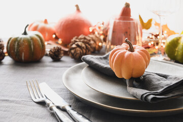 Thanksgiving day table setting decorated fallen leaves, pumpkins on gray linen tablecloth. Close up.