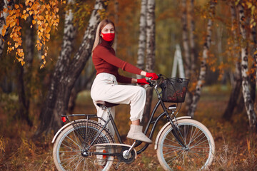 Fototapeta na wymiar Young woman riding bicycle in red gloves and face mask at autumn park.