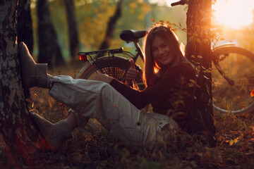 Happy active young woman sitting near vintage bicycle bike in autumn park at sunset. European...