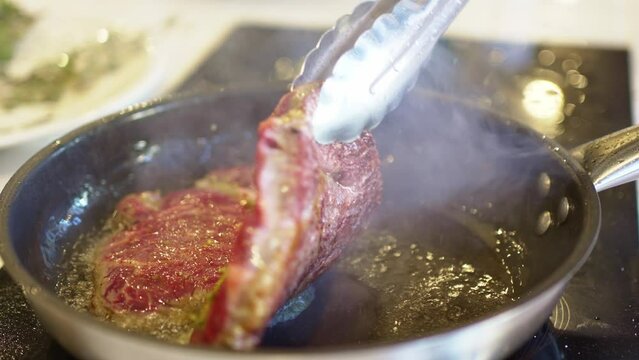 in a hot frying pan fry pieces of meat with garlic and rosemary. cooking steaks.