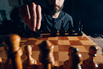 Young adult handsome man playing chess in dark with side lit.