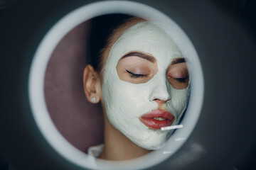 Young beautiful woman receiving facial clay mask in spa beauty salon.