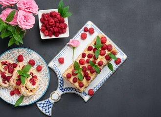 Baked meringue roll with cream and fresh red raspberry on a black wooden board