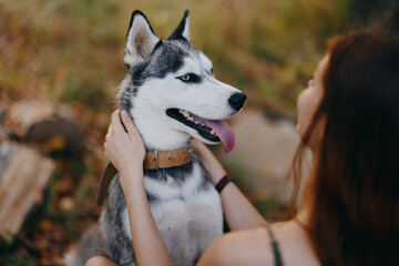 A woman with a husky dog ​​sits with her back to the camera strokes her beloved dog while...