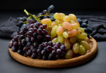 Black and green grapes in a wooden round plate on a black table