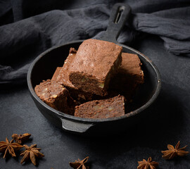 Pieces of baked brownie in a metal black frying pan on the table