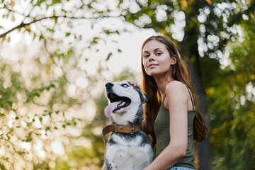 A woman walks with her husky dog ​​in nature in a park among trees and smiles stroking the dog, lifestyle real friends