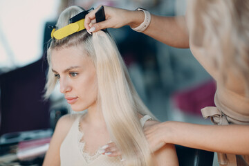 Hairdresser female making hair extensions to young woman with blonde hair in beauty salon. Professional hair extension