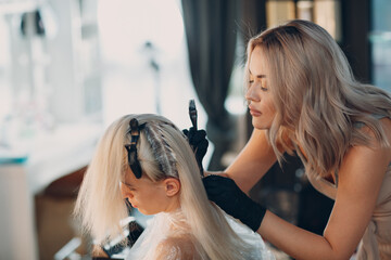 Young woman hairdresser dying hair at beauty salon. Professional hair roots coloring.