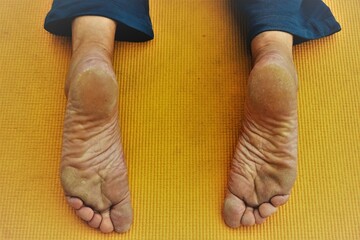 Füße von auf Bauch liegender Frau auf gelber Gummimatte mit blauer Jogginghose beim Yogatraining