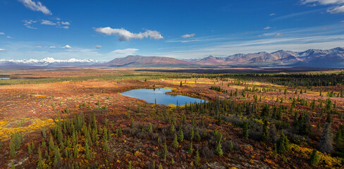 Aerial view of Alaska Range with a lake and autumn tundra in foreground with blue sky.