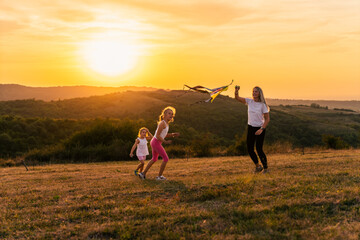 Happy family playing outdoors. Mother and children run across the meadow with a kite. sunset time. golden hour. family concept.