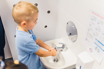 Toddler boy washing his hands with soap after playtime at the nursery school. Concept of early healthy hygiene learning for kids wellness. High quality photo