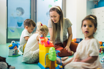 Nursery school. Toddlers and their teacher playing with colorful plastic playhouses, cars and boats. Imagination, creativity, fine motor and gross motor skills development. High quality photo