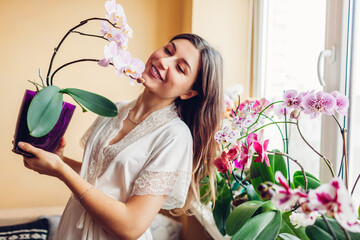 Portrait of woman admiring blooming phalaenopsis orchid holding pot. Gardener takes care of home...