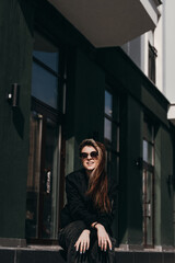 a young girl in glasses sits on the street near the building