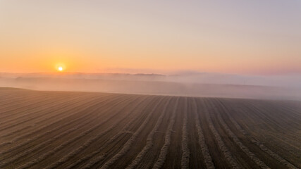 Brown farm field with fog-covered horizon and bright orange rising sun. Colorful morning sky. Landcape of Roztocze Poland. Horizontal shot. High quality photo