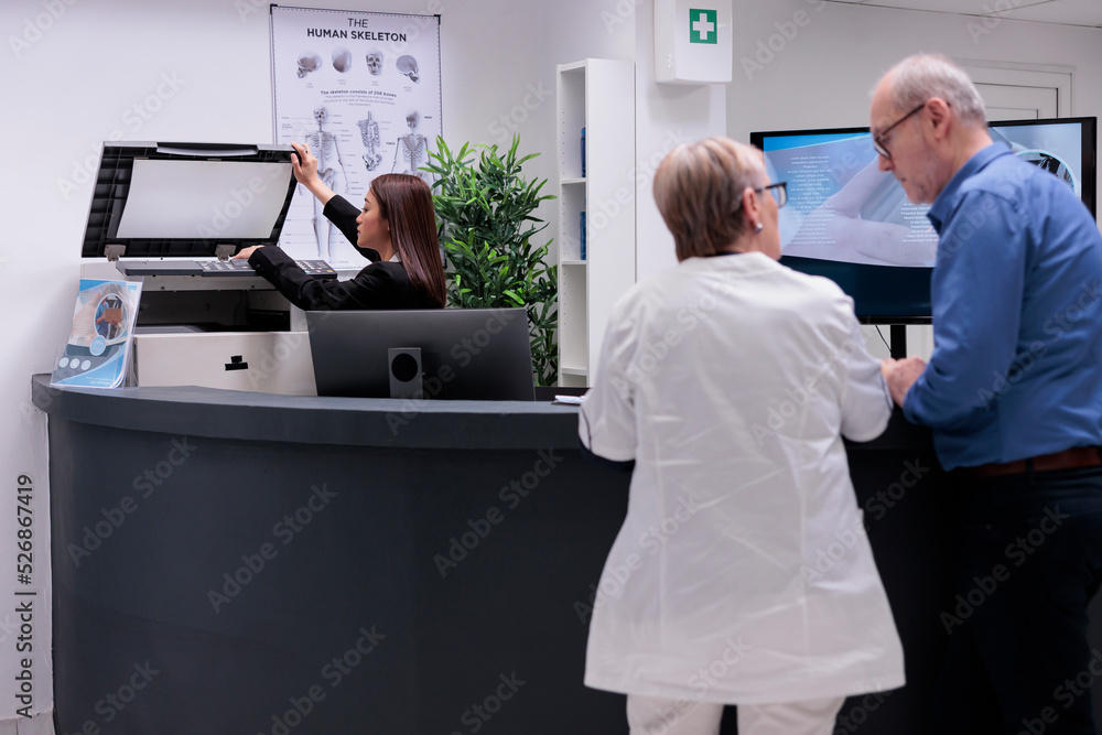 Poster worker using copy printer at reception desk to make report papers before checkup consultations. woma