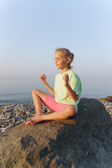Fototapeta na wymiar The girl is sitting on the beach and doing yoga, meditating.