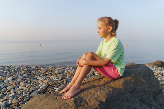 A girl is sitting on a rock by the sea and meditating.
