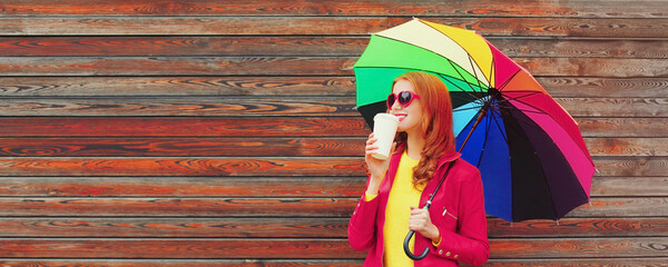 Autumn portrait of happy smiling young woman with colorful umbrella and cup of coffee wearing red...