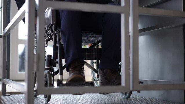 Unrecognizable man riding wheelchair on elevator platform indoors. Front view ill Caucasian guy using accessibility lift in building