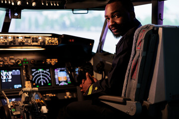 Portrait of african american pilot using dashboard command in cabin to takeoff with plane jet and fly. Male aviator in airways uniform pushing control panel buttons and power lever.