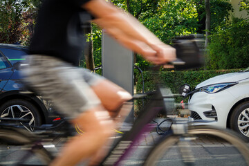 Two e-cars at a charging station, a cyclist is passing in the foreground