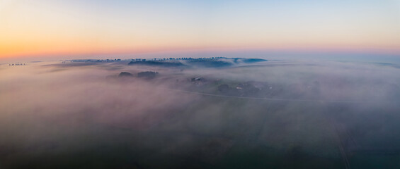 Fototapeta premium Colorful sunrise and thick fog over vast farm fields of Roztocze Poland. Nature and agriculture. Wide horizontal shot. High quality photo