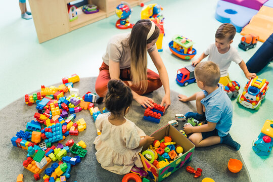 Playtime at nursery school. Toddlers with their teacher sitting on the floor and playing with building blocks, colorful cars and other toys. High quality photo