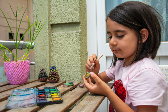 Elementary school girl paints pinecones on the balcony