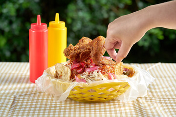 Mano tomando una tajada de platano de un plato con Pollo firto servido en una canasta de plastico
