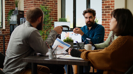 Business manager analyzing charts on laptop and working with colleagues, brainstorming ideas to find data research solution and plan presentation. Coworkers using documents and network.