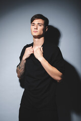 A guy of model appearance in black clothes poses on a gray studio background. Male fashion portrait