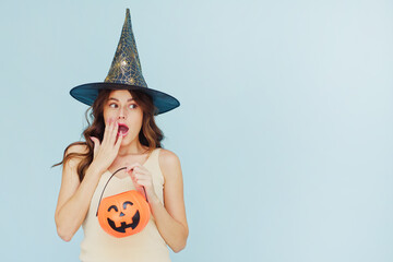 Young beautiful excited woman in a witch hat holds a basket pumpkin and looks away. Wow, Halloween sale