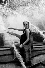 Fototapeta premium Happy woman having fun at the city fountain on a summer day.