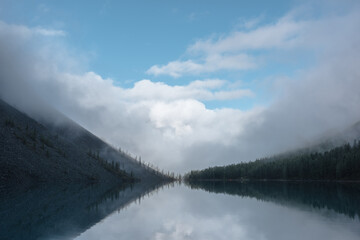 Tranquil meditative misty scenery of glacial lake with reflection of pointy fir tops and clouds at...