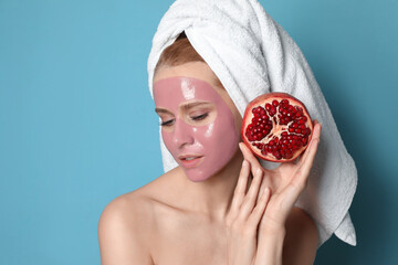 Young woman with pomegranate face mask and fresh fruit on light blue background