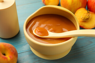 Bowl and spoon with tasty pureed baby food on light blue wooden table, closeup