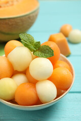 Melon balls and mint in bowl on light blue table, closeup