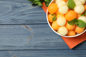 Melon balls and mint in bowl on blue wooden table, top view. Space for text