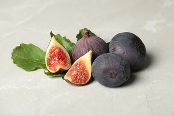 Tasty raw figs and green leaf on light grey marble table, closeup