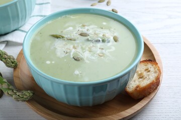 Bowl of delicious asparagus soup served on white wooden table